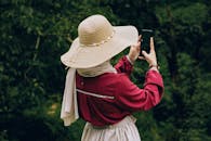 A woman in a straw hat takes a selfie in a lush green outdoor setting, capturing the essence of fashion and nature.