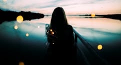 A woman holding lights, silhouetted against a serene lake at twilight.